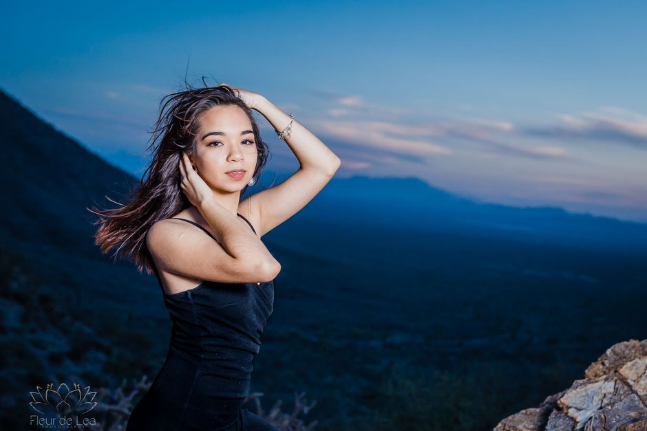 Senior girl posting in front of mountain sunset, wind blowing hair.  Fleur de Lea Photography
