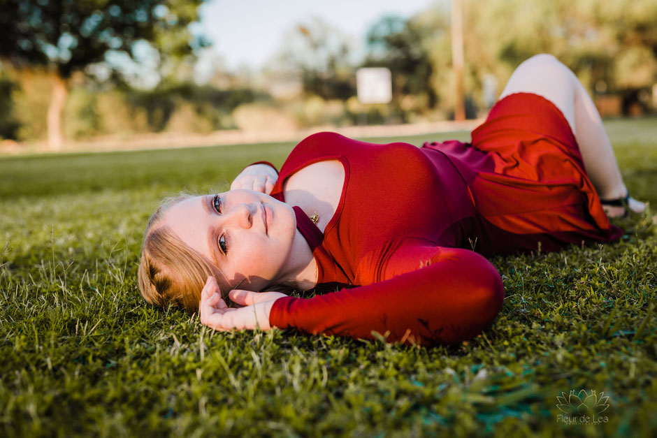 senior girl in red dress laying in green grass. Fleur de Lea Photography