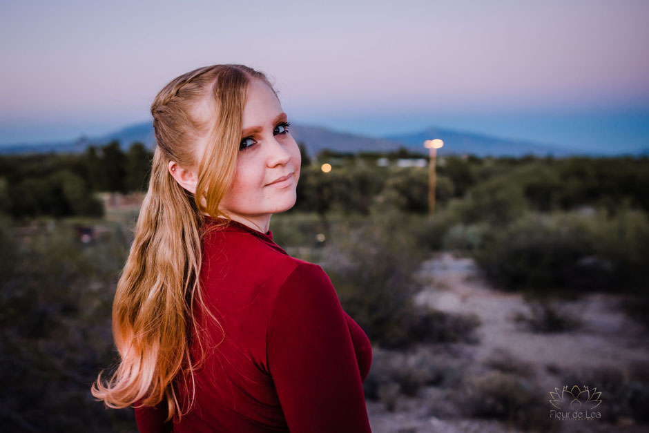 senior girl strawberry blonde in red dress pose over shoulder during cotton candy sunset. Fleur de Lea Photography