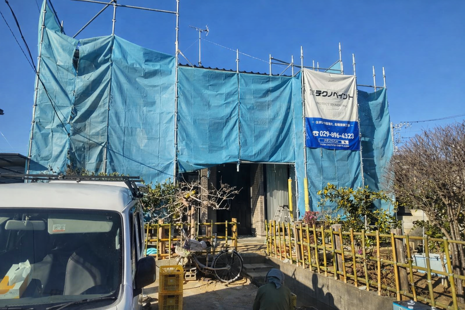 外壁塗装中家、足場と養生ネットが設置され、「テクノペイント」の現場シートが設置されている