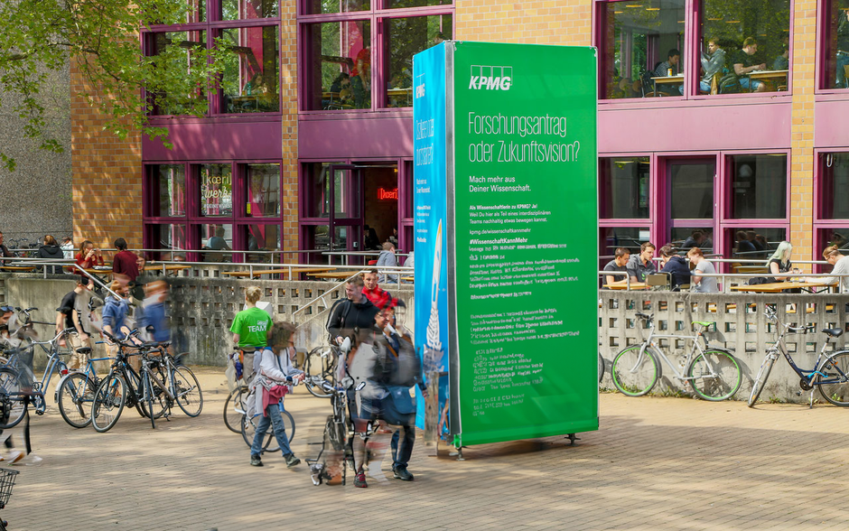 Eine Gruppe junger Leute steht vor einem Campus Tower Werbeturm