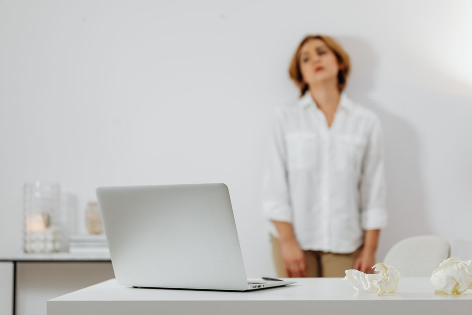 Frau steht gestresst vor ihrem Schreibtisch mit Laptop