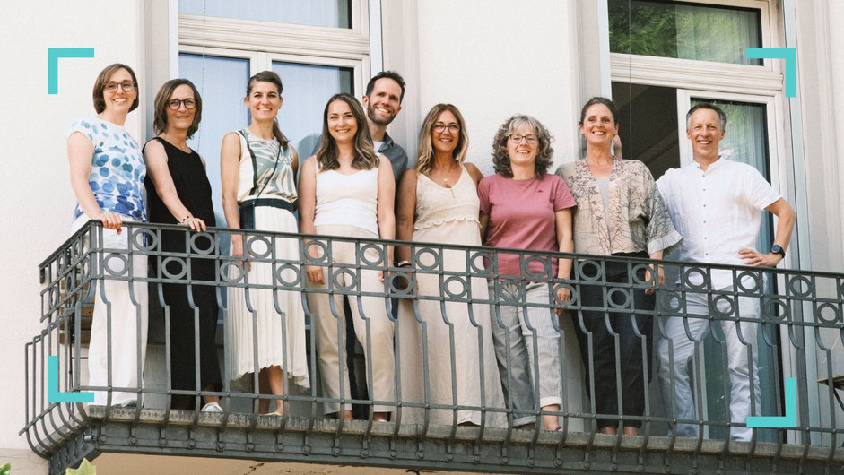 Das Team von Neuro im Zentrum steht auf einem Balkon. Neurologen und Neuropsychologen und Praxisassistenz