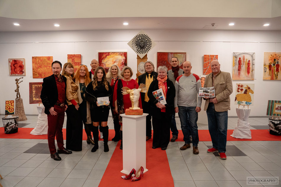 Ganz in Gold und Rot erstrahlte das Foyer des Kunsthauses Mikizzaner bei der Weihnachtsausstellung im Dezember 2024. Am Foto: Die anwesenden Künstlerinnen und Künstler, darunter Arthena Maxx, der Grazer MaLo und der Popartkünstler Hannes Rossbacher.