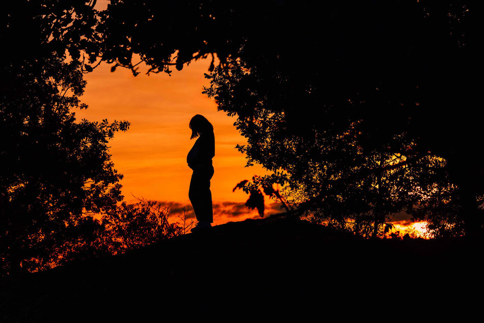 Silhouetten-Bild einer schwangeren Frau bei Babybauchshooting im Sonnenuntergang.