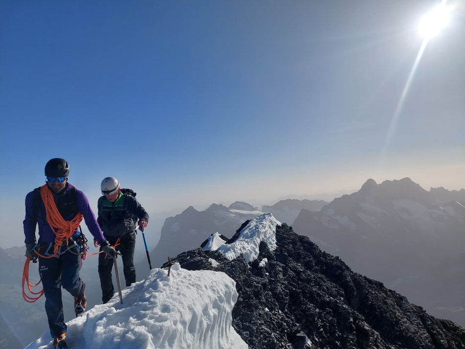 Bergführer hat mit seinem Gast den Berggipfel erreicht bei strahlendem Sonnenschein