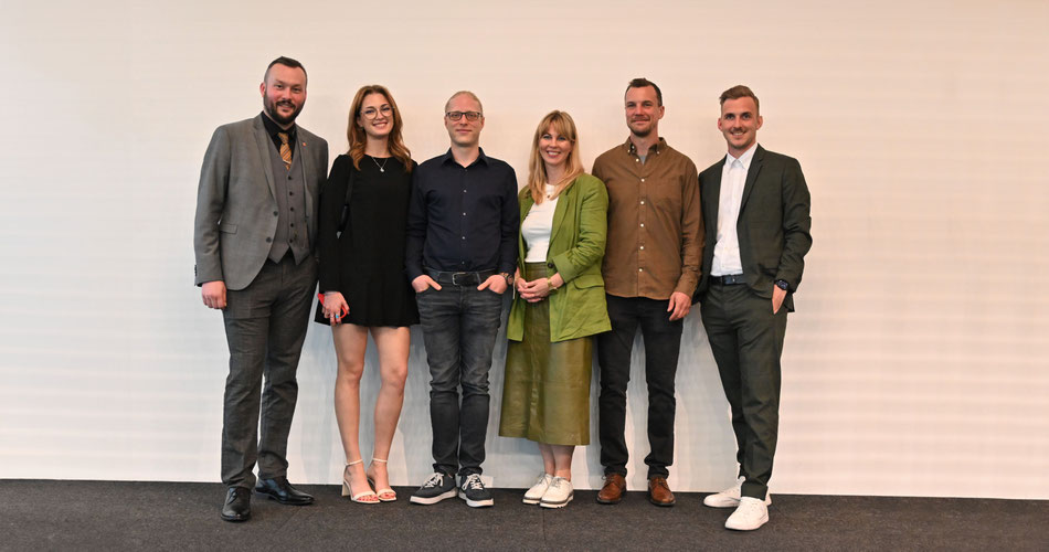Sechs Teilnehmer:innen stehen für ein Gruppenfoto vor einer weißen Wand.