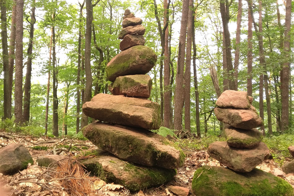 2 Steinpyramiden im Wald, eine größere mittig, rechts eine kleinere