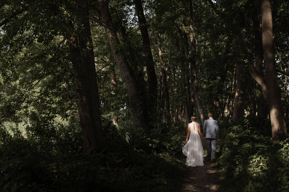 Ein Brautpaar hält sich an den Händen und geht durch den Wald.