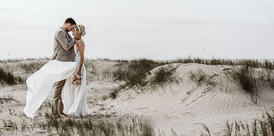 Brautpaar am Strand nach einer freien Trauung mit Constanze Marienfeld, beide Hand in Hand, Meer und Himmel im Hintergrund