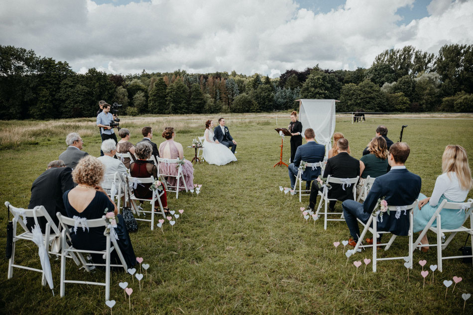 Gäste auf der Wiese, das Brautpaar glücklich, Constanze liest ihre Rede vor, im Hintergrund sind Pferde auf der Koppel