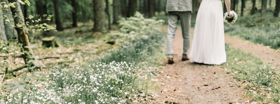 Hochzeitspaar läuft auf einem Waldweg, Blumen wachsen am Wegesrand