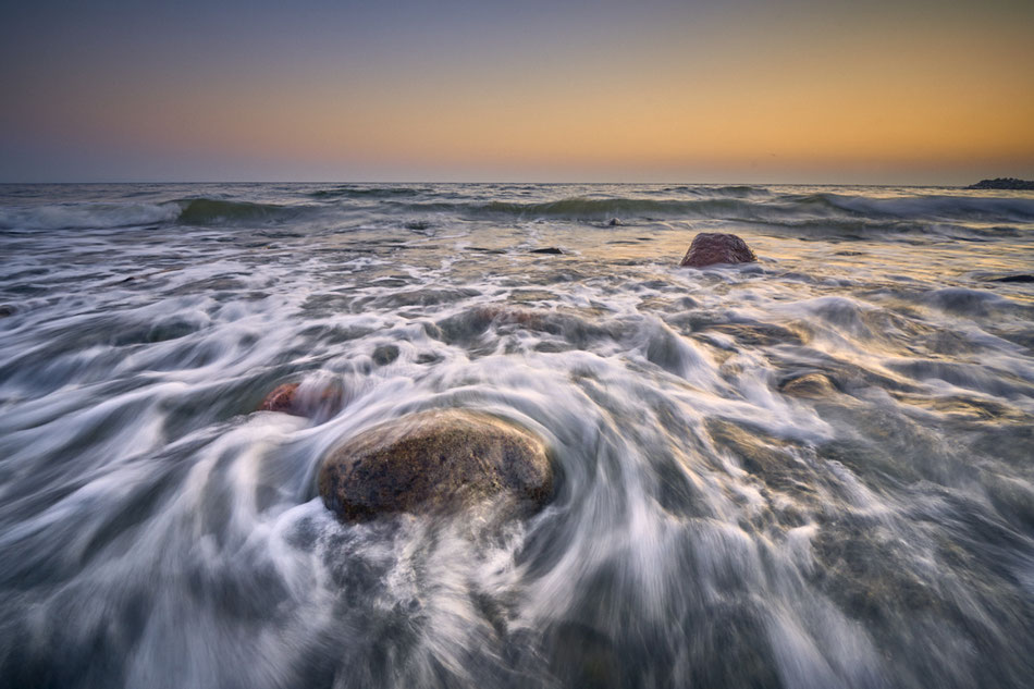 Wellen, die über Felsen an einem Strand bei Sonnenaufgang fließen