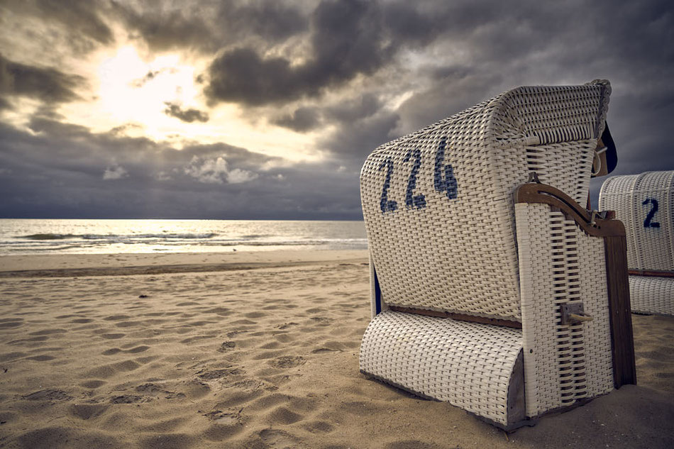Strandkorb mit der Nummer 224 auf einem Sandstrand bei bewölktem Himmel und Sonnenaufgang am Meer