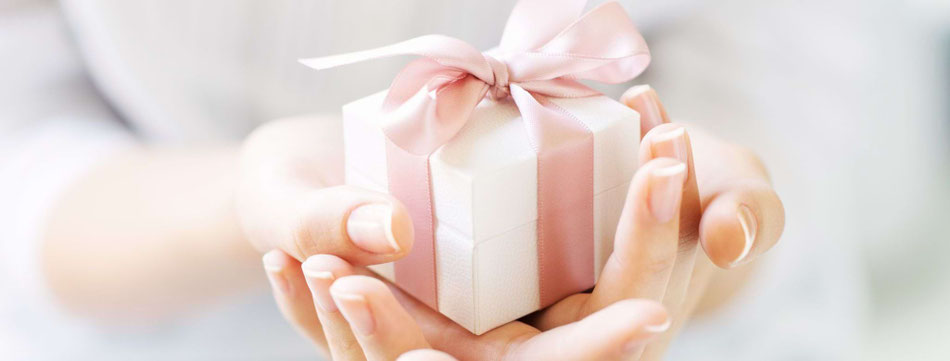 Nahaufnahme von Händen, die ein kleines, weißes Geschenk mit rosa Schleife halten – Symbol für Wertschätzung und liebevolles Schenken.
