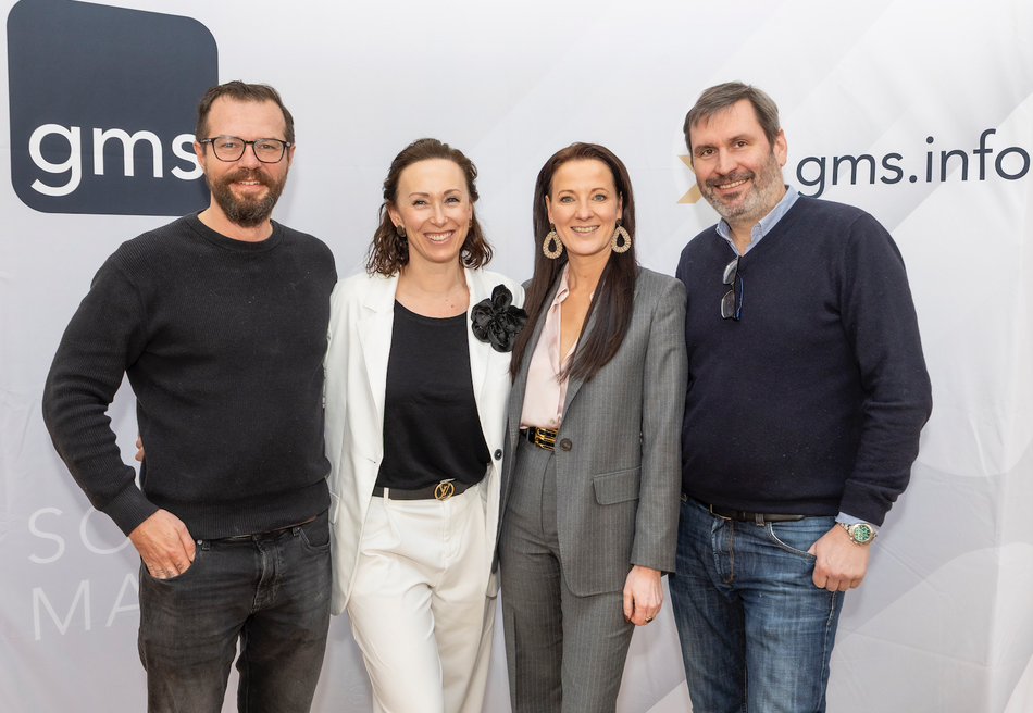 Vier Teilnehmende posieren lächelnd vor einer GMS-Wand beim IT Gipfel 2026.