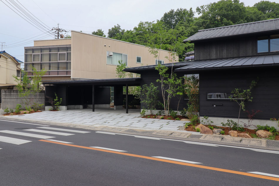 外構床は白御影石張り。縦のみ目地を広げてダイカンドラの緑をみせている。背後の山の緑と庭木が連続していく。