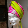 Sur l'image, un chapeau en forme conique pour femme en tissu rose vif avec un bandeau en vert lime et une broche sur le haut. Création unique de la maison de couture Fil et Paillettes. 