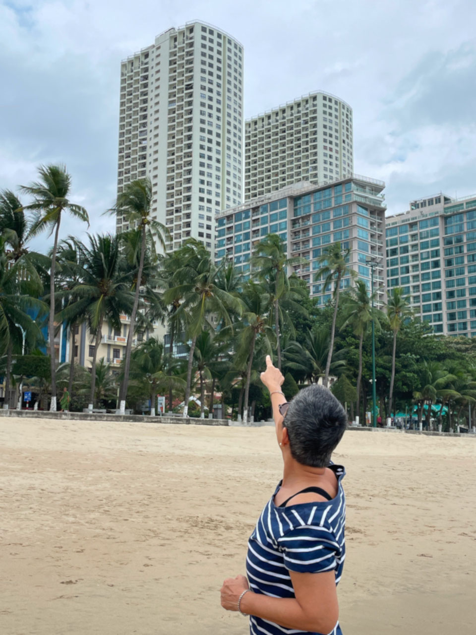 Person zeigt am Strand von Nha Trang auf ein Wohngebäude