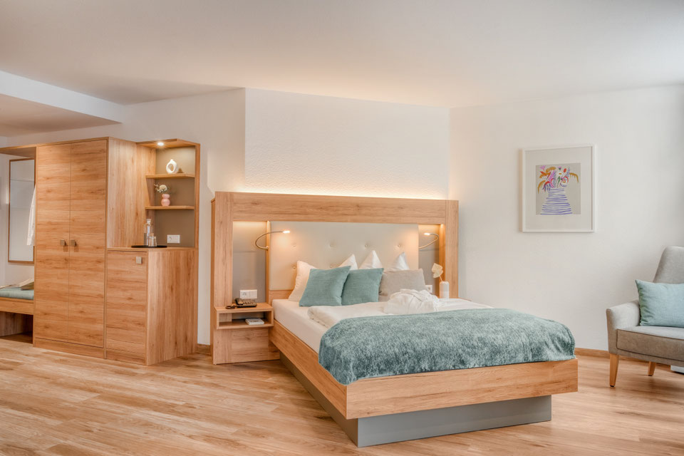 Neue Patientenzimmer, mit warmen Holzmöbeln und türkisen Farbakzenten.