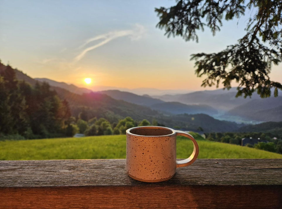 Handgemaakte whitewashed mok op het balkon in Slovenië met zonsopkomst en bergen op de achtergrond, een ochtendritueel tijdens slow travel