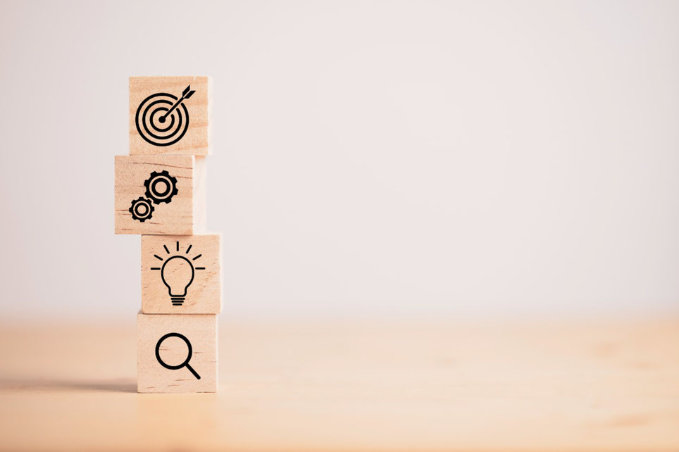 Ein Bild mit vier aufeinander gestapelten Holzklötzen mit Symbolen für Ideen, Ziele und Kreativität