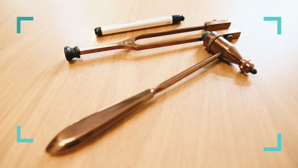 Neurologische Untersuchungsinstrumente – Reflexhammer, Stimmgabel und Stift auf Holztisch – Symbolbild für neurologische Diagnostik und Patientenfragen in der Praxis Neuro im Zentrum St. Gallen