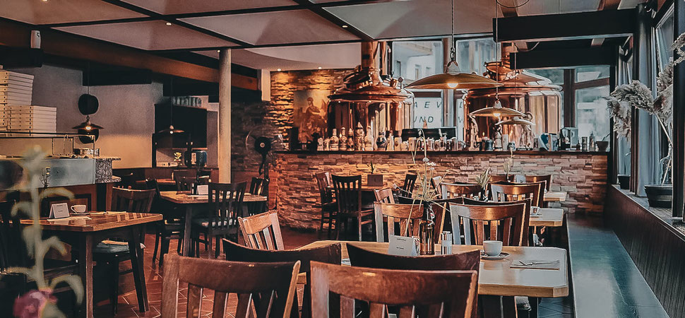 Accogliente ristorante-birreria con tavoli in legno, caldaie di rame e luci soffuse nel Martinerhof a San Martino in Passiria, Alto Adige.