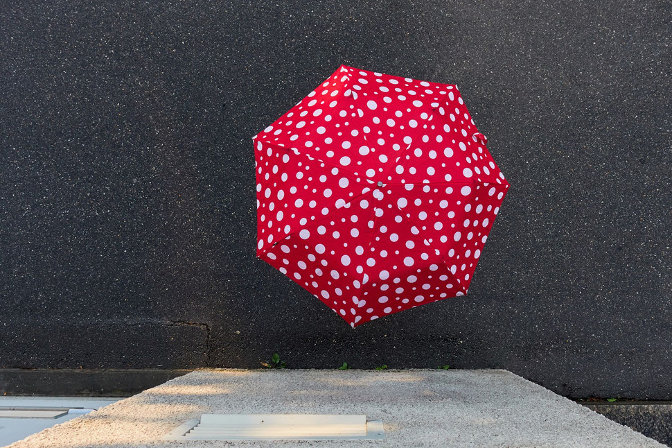 The image shows the photograph of a red umbrella with white dots from above.