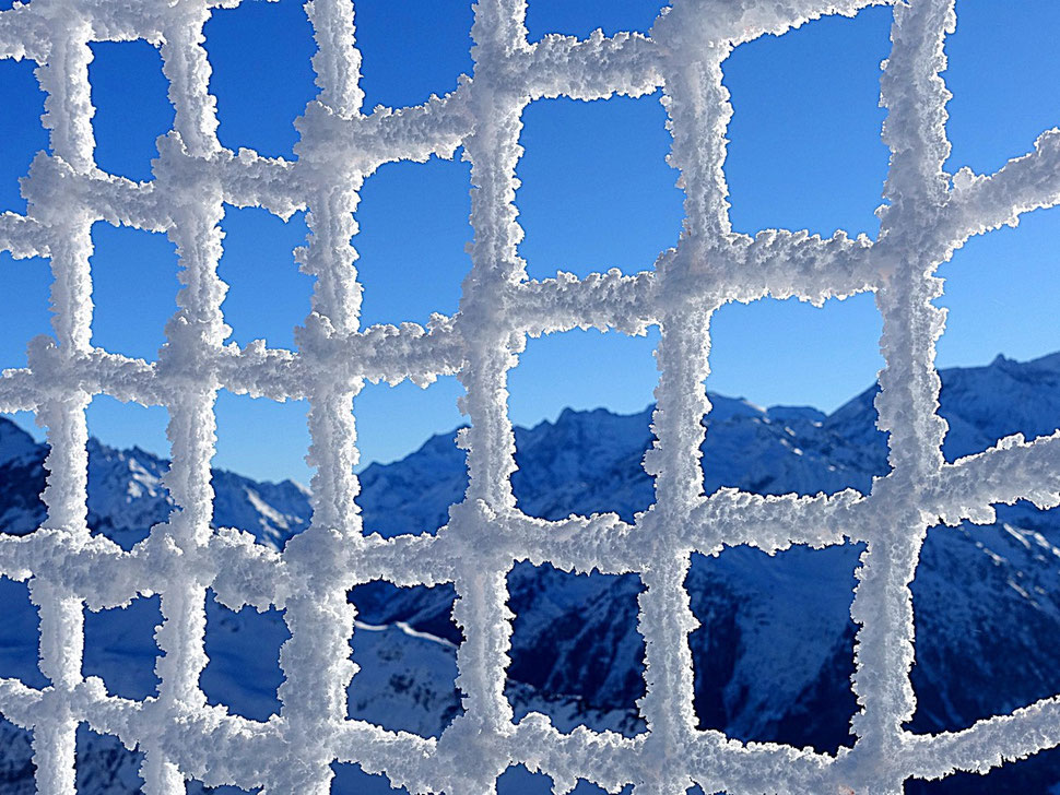 The image shows the photography of a snow covered safety net with some mountains and a snippet of blue skies in the background. 