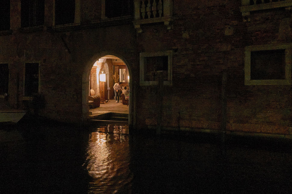 The photograph shows - through an open door of a building in Venice - two men sharing something on a smartphone. 