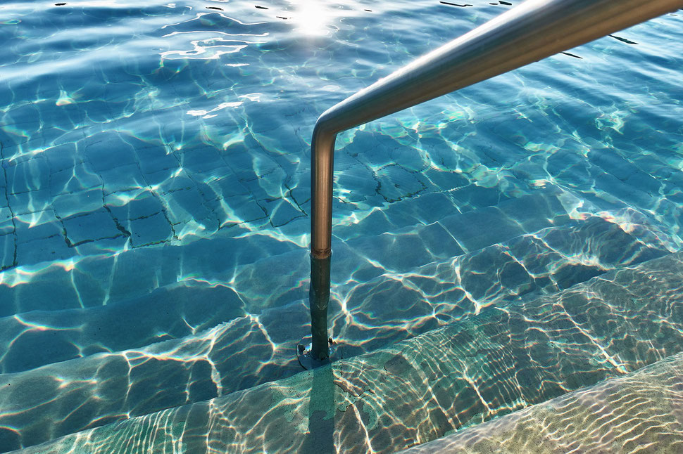 The image shows the photograph of a snippet of a swimming pool illuminated by evening sunlight.