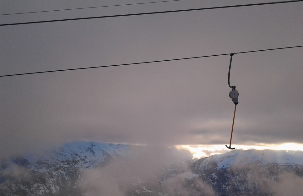 The photograph shows an image of a single ski lift ironing against the backdrop of mountains, clouds and a shimmer of sunlight.