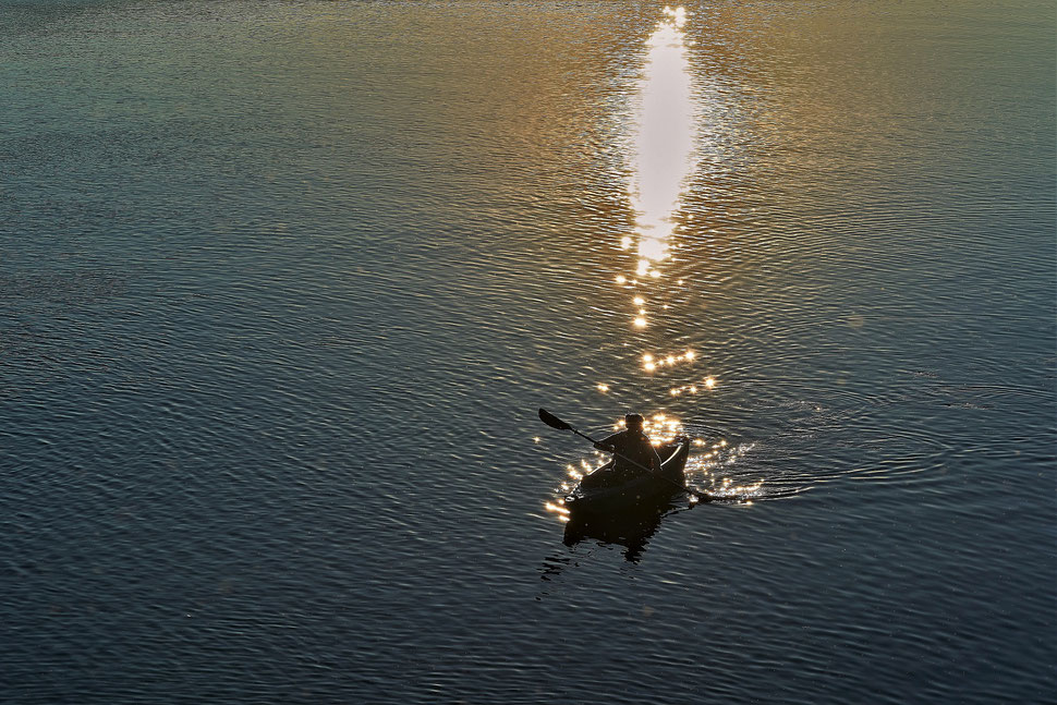 The image shows a photograph of a canoer on a lake during sunset. The beautiful sunlight is reflected on the surface of the water.