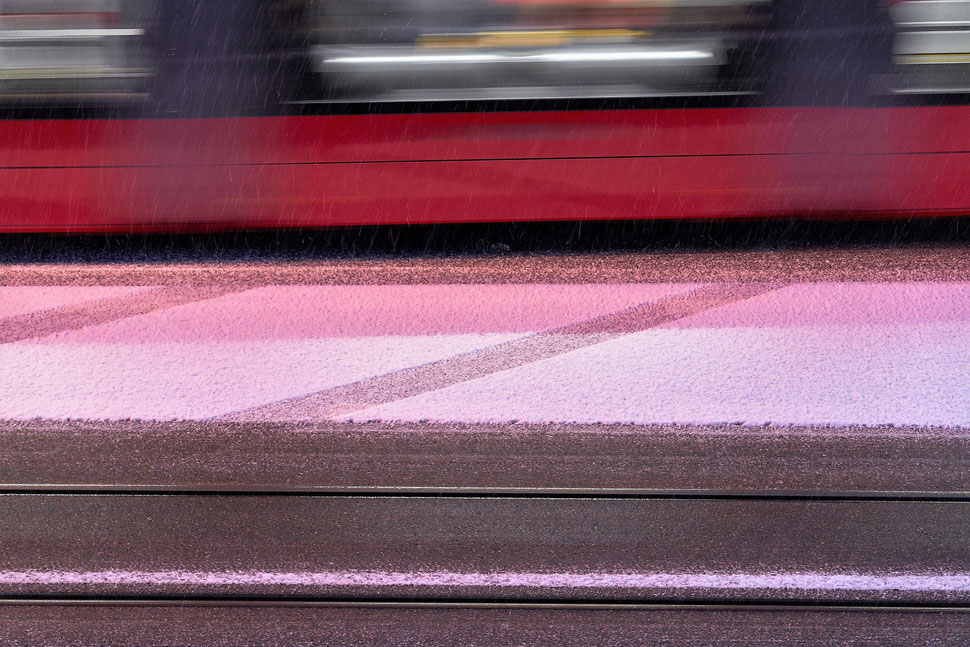 The image shows the photograph of part of a passing red tram and the snow covered street in Winter.