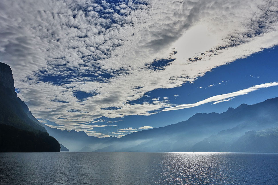 The image shows the photograph of a landscape with a lake, mountains, blue skies and white clouds. The predominant color is blue.