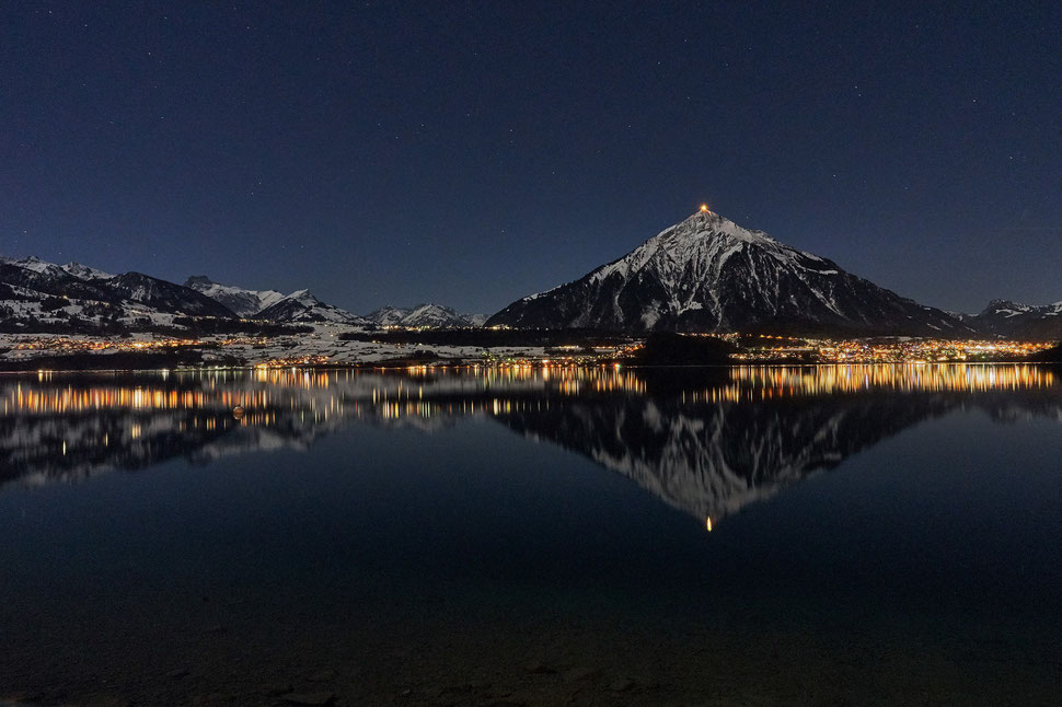 The image shows the nocturnal photograph of the Niesen and its reflection in Lake Thun.