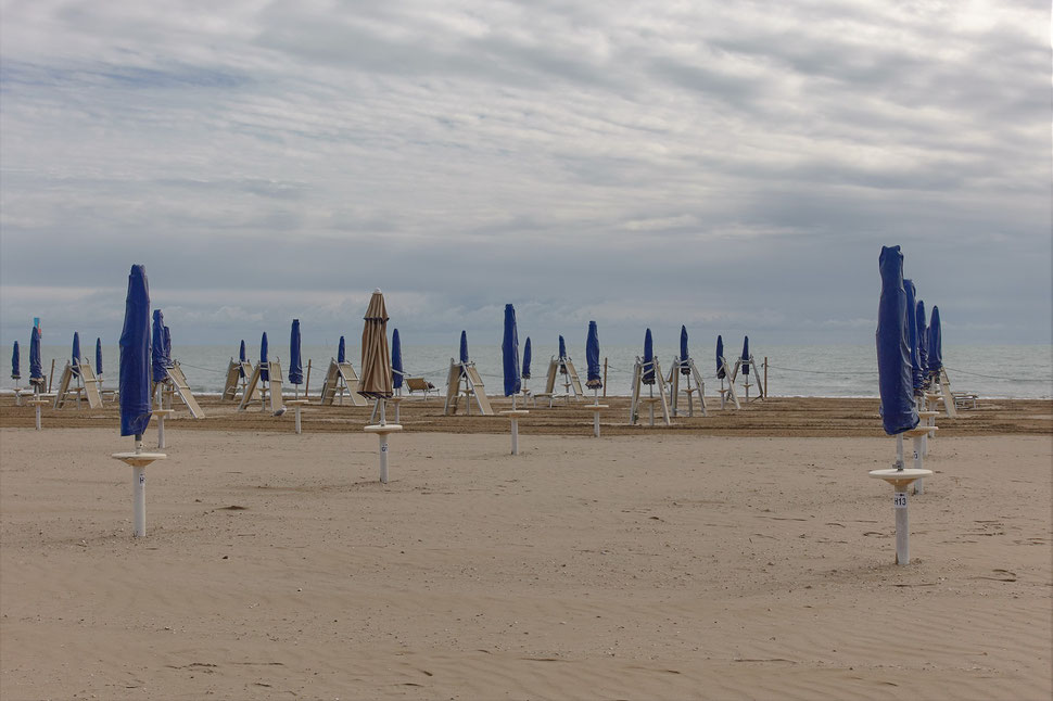 The image shows the photograph of a sand beach with rows of folded parasols.
