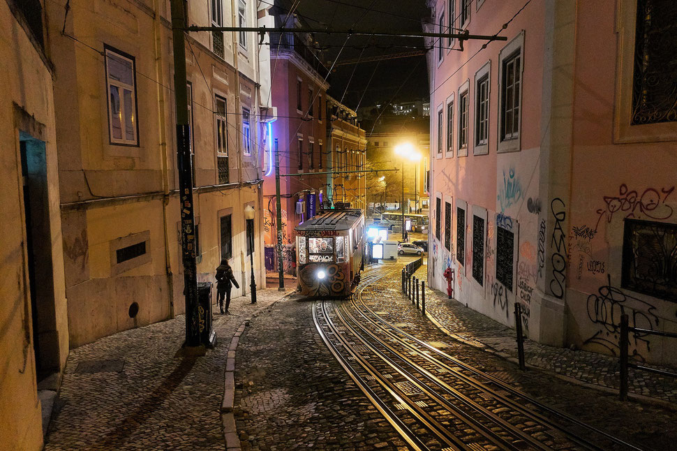 The Image shows a photograph of a street and a tram in Lisbon by night.