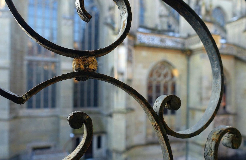 The photograph shows an image of wrought iron window grilles in the foreground and the walls and windows of the bernese cathedral in the background.  Bild von Bern.