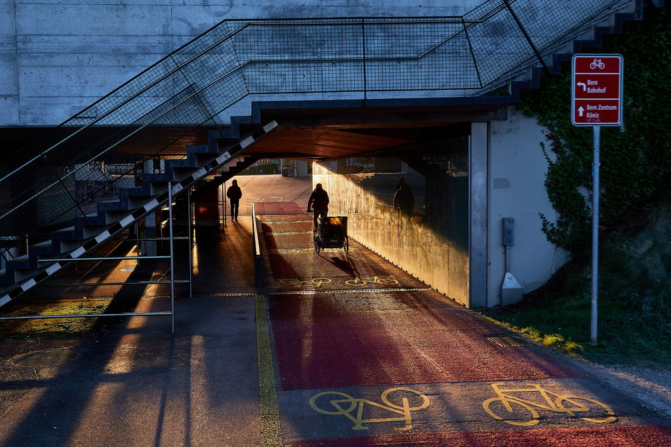 The image shows a photo of a bicycle with a trailer riding on a cycle path through an underpass into the beautiful morning sunshine.