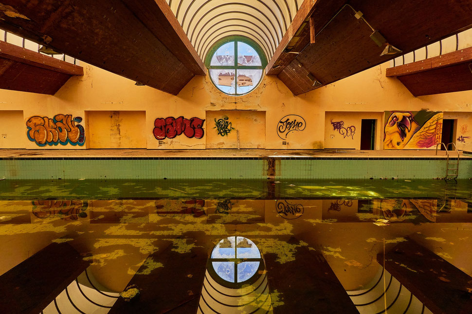 The image shows a photograph of a derelict swimming pool in an abandoned thermal spa.