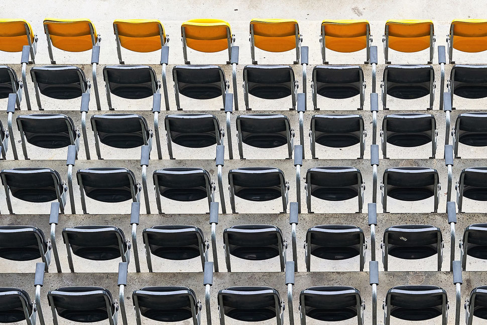 The image shows the photograph of black chairs in a football stadium. The front row of chairs is yellow.