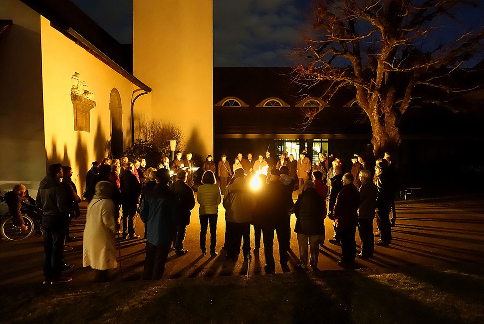 The image shows a night photograph of people gathering around a fire in front of the protestant church in Bümpliz.