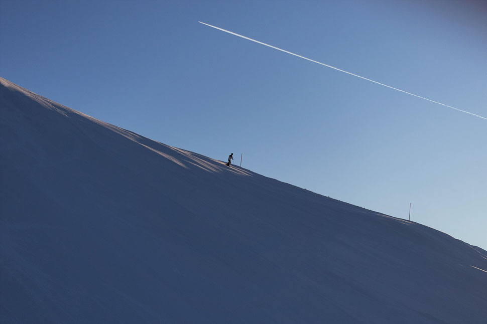 The image shows the photograph of a single skier on an empty slope and under a blue cloudless sky.