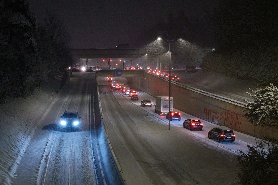 The image shows a night photograph of a three streets with heavy traffic, a bridge and traffic lights during a snowstorm.