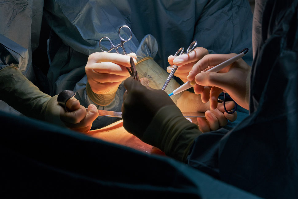 The image shows three pair of hands with sugical instruments performing a surgery.