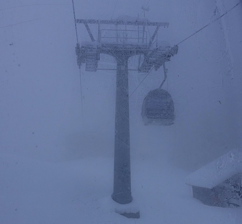 The photograph shows an image of a gondola that is crossing a mast  in a surrounding of thick fog an snow. 