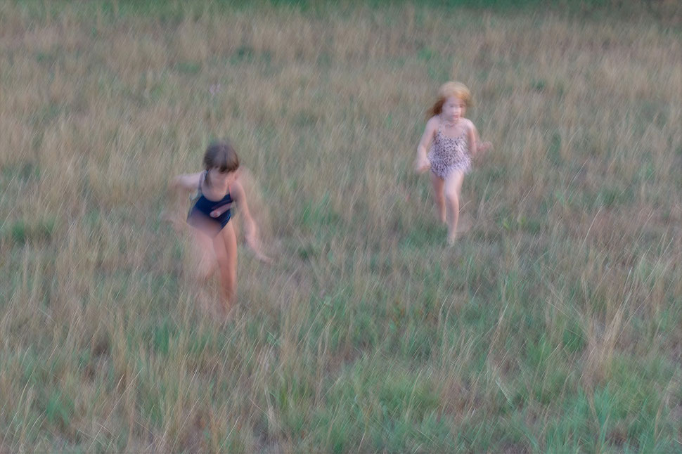 The image shows a blurry photograph of two little girls running through a field of grass.