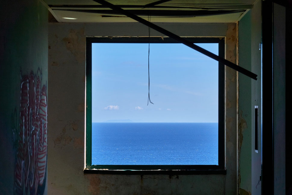 The image shows a photograph of a glassless window in a derelict abandoned building.